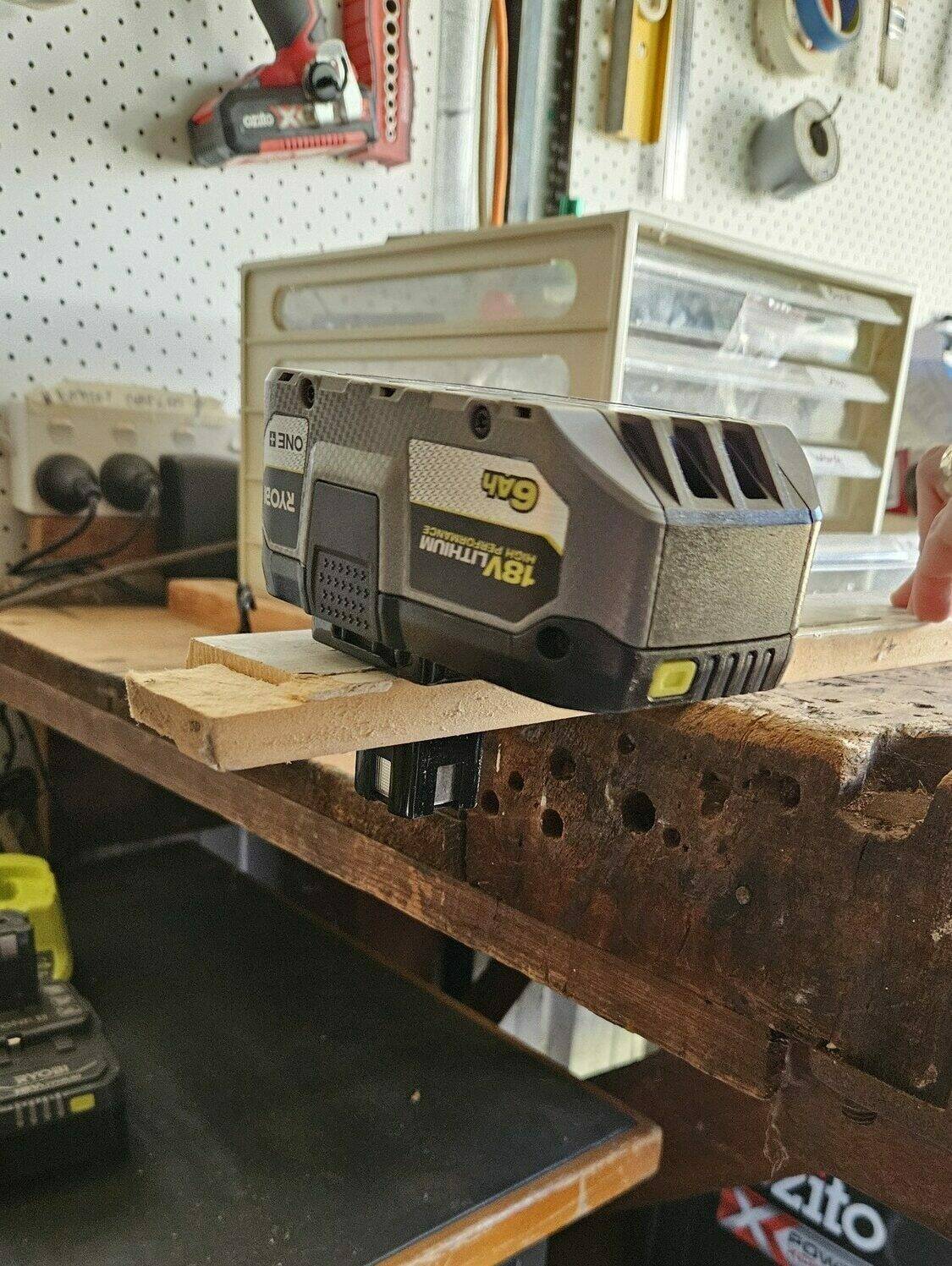 A Ryobi battery slotted into a scrap piece of wood, which has had a hole drilled out of it.