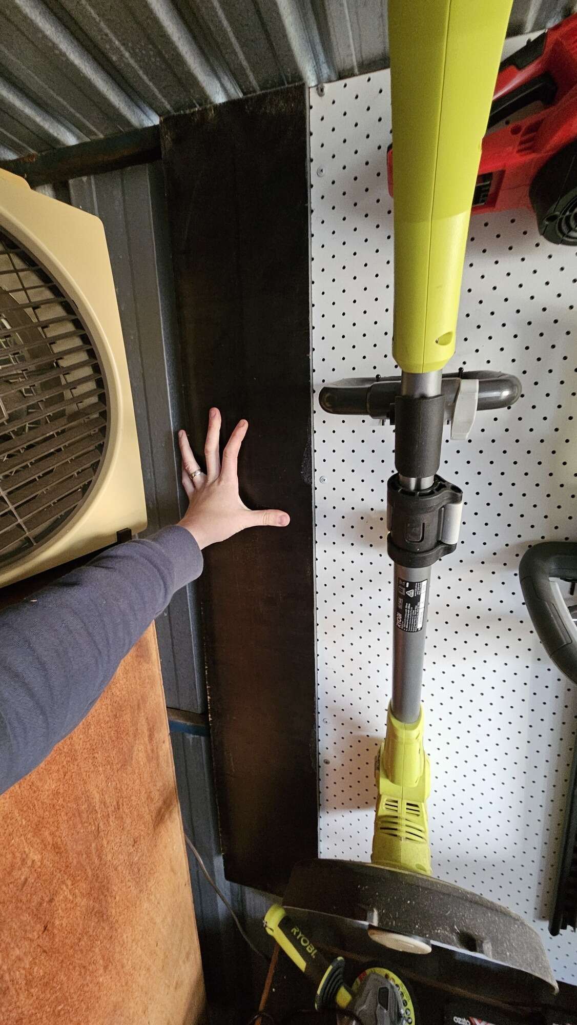 My hand holding up a long piece of wood onto my shed wall