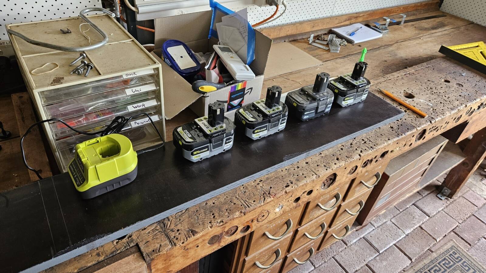 4 Ryobi batteries and a charger arranged on a rectangular piece of wood. The batteries are in one line, showing I can fit a grid of 2x4 batteries. The charger is below the batteries.