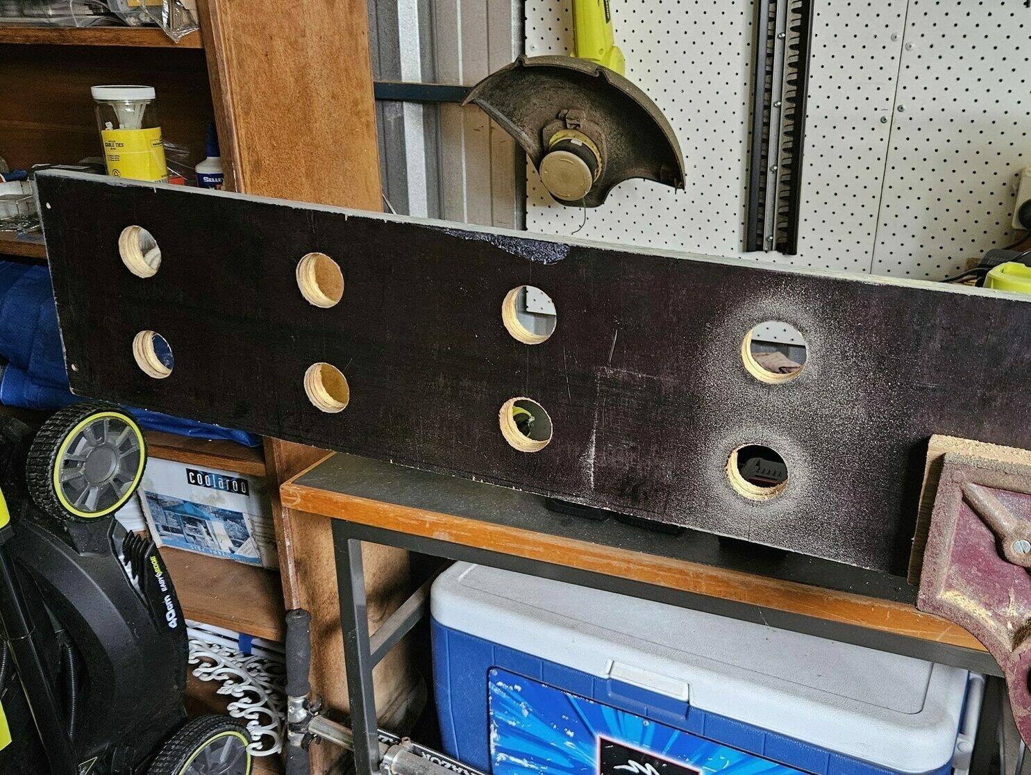 The long wooden board being held in a vice. It has 8 holes drilled in an even 2x4 grid.