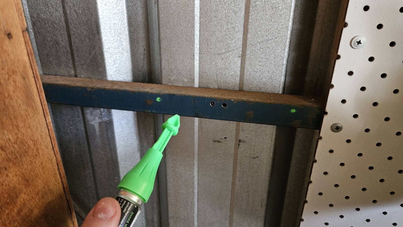 One of the metal beams of my shed with 2 dots marked on it. A marking tool is shown as well, which is the same colour as the dots it made (green).