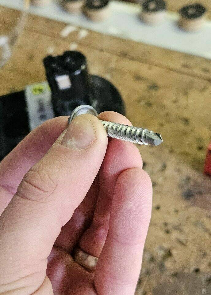 A close up of my holding a self-drilling screw. It has threads most of the way down, but its tip is shaped like a drill bit.