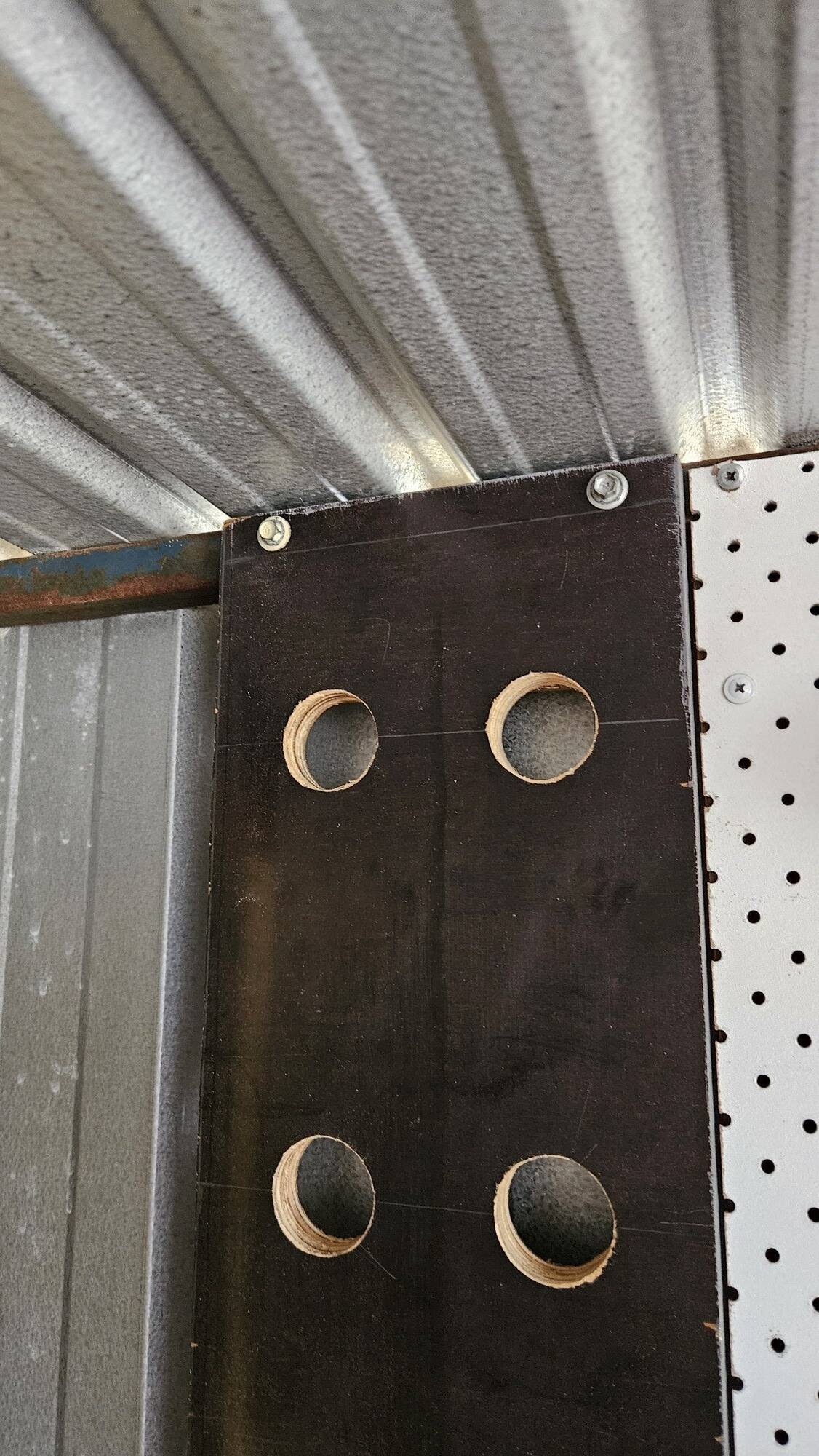 The top of the wooden board, now mounted to the shed wall. Two screw heads are at the top in line with the top metal frame.