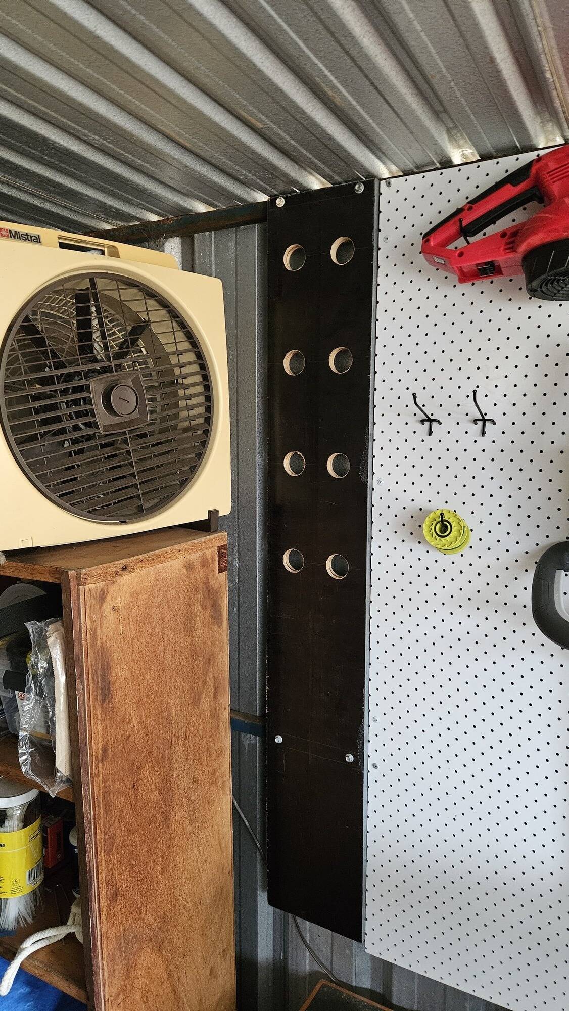 The whole wooden board, now mounted to the shed wall. It sits between a shelf on one side and flush with a pegboard on the other side.