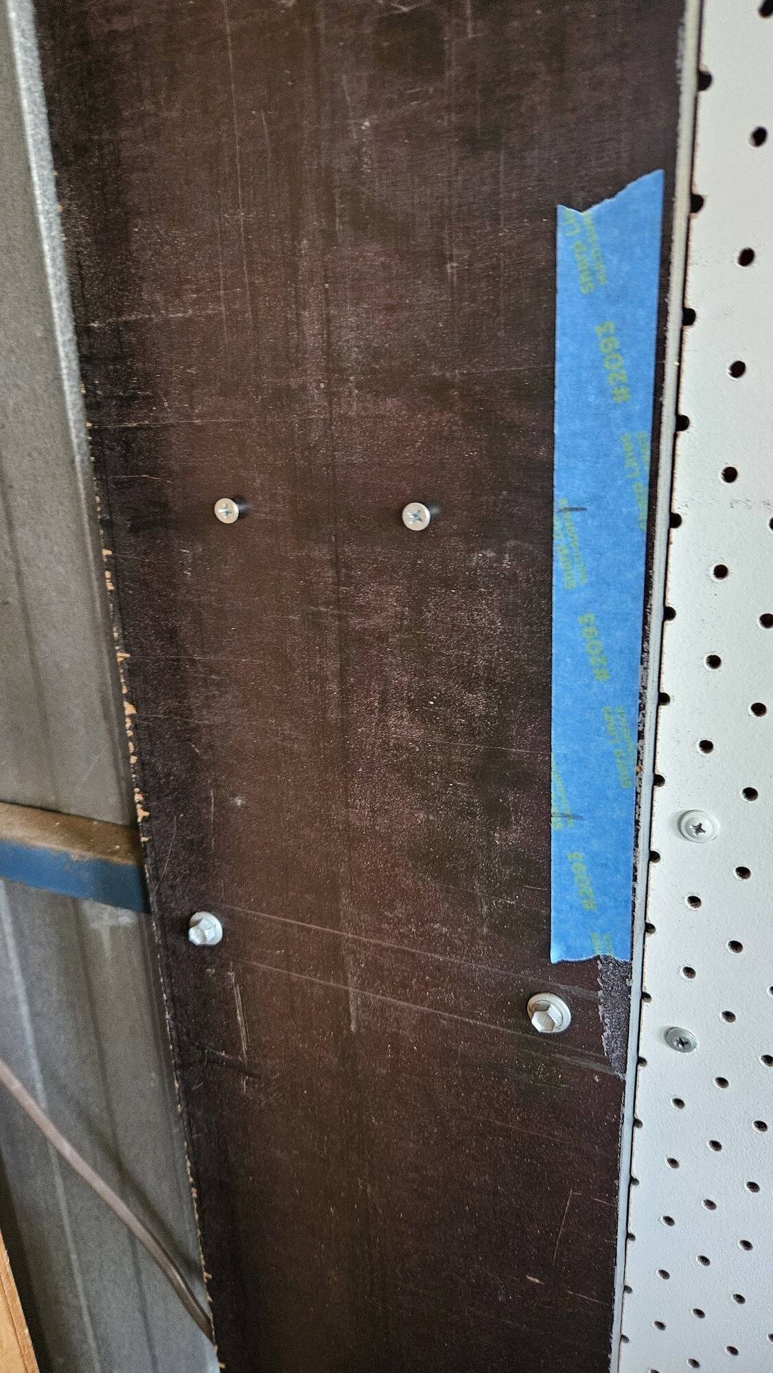 The wooden board with two screws placed horizontally in the middle. Tape is on the side with markings which line up with the screws.