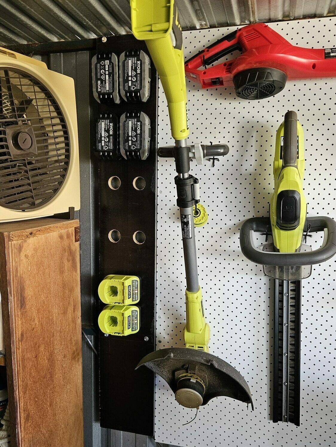 The wooden board in place with batteries slotted in and chargers mounted. Power tools are off to the side on the pegboard.