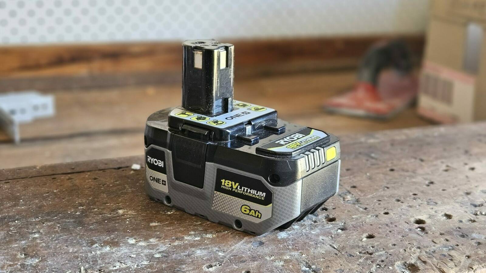 A Ryobi battery sitting on my workbench, showing its shape - it has a solid, rectangular base with a cylindrical stalk protruding upwards from the rear.